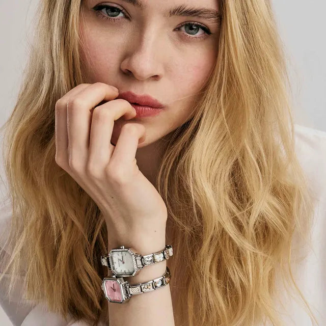 Woman wearing two silver watches with a plain background