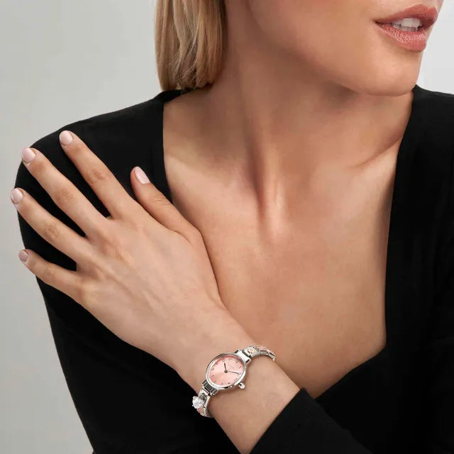 Woman wearing a silver watch with a pink face on a neutral background
