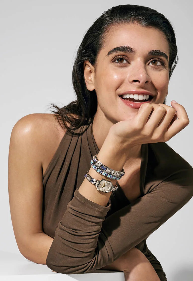 Woman wearing multiple bracelets and a watch on a plain background